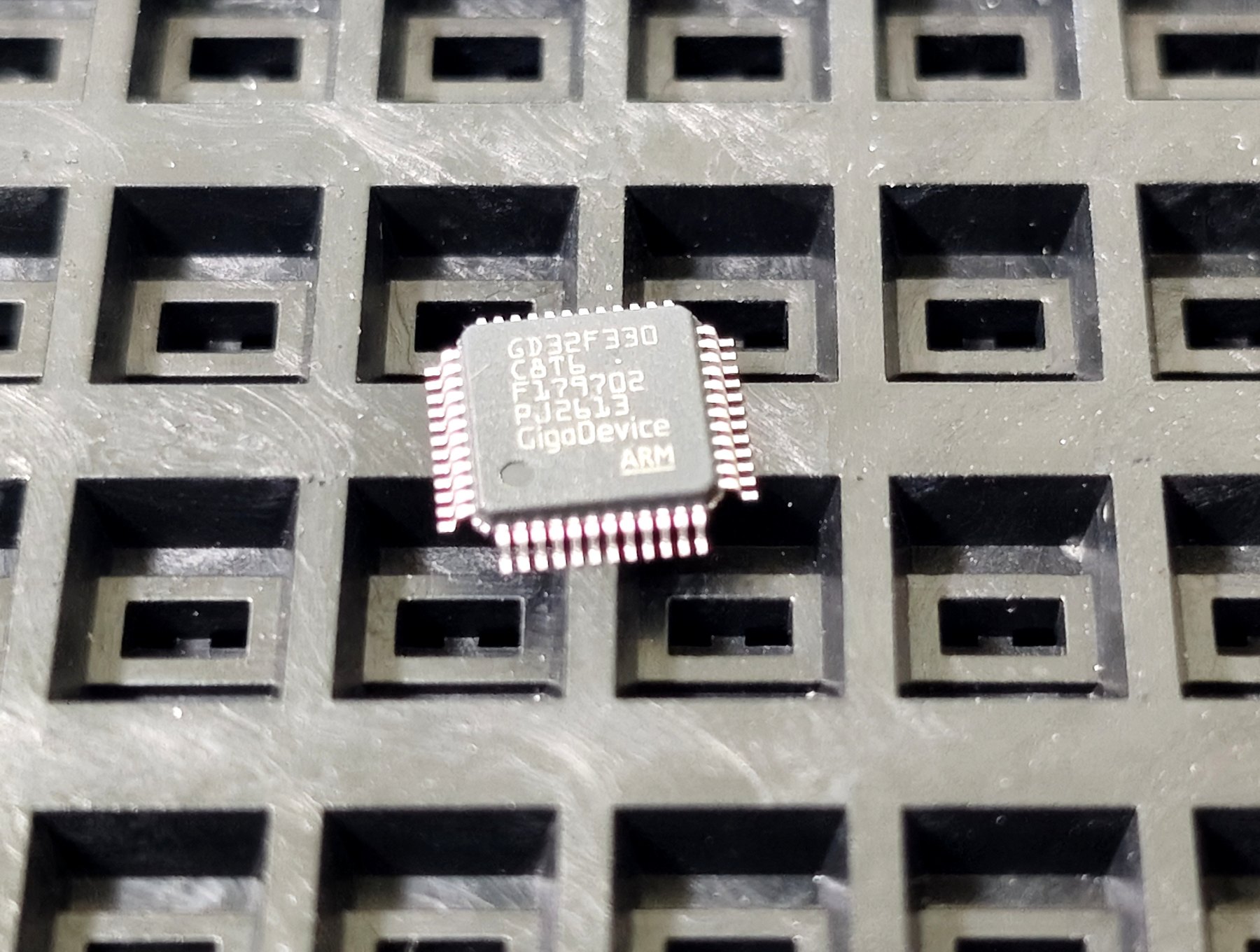 Close-up of a GigaDevice microcontroller in a waffle tray, with the full part number, lot code and date code legible.